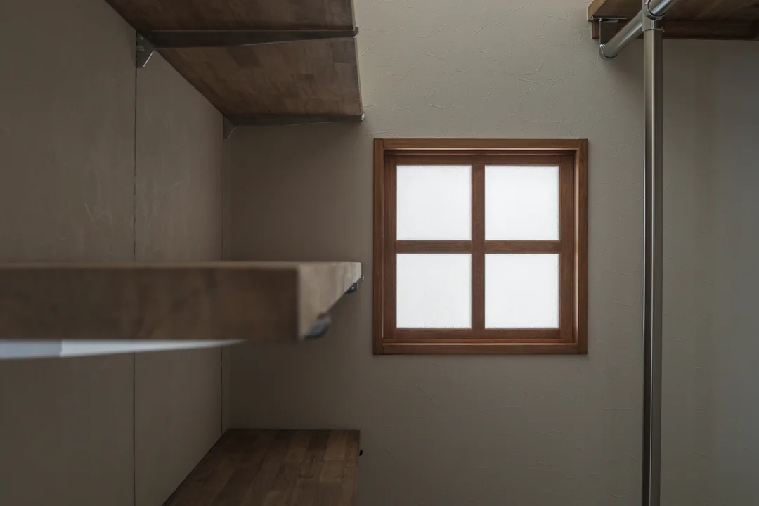 左手前に棚板。奥の壁に四角い窓。窓の木枠は田の字になっている。窓の右側には円柱型のハンガーバー