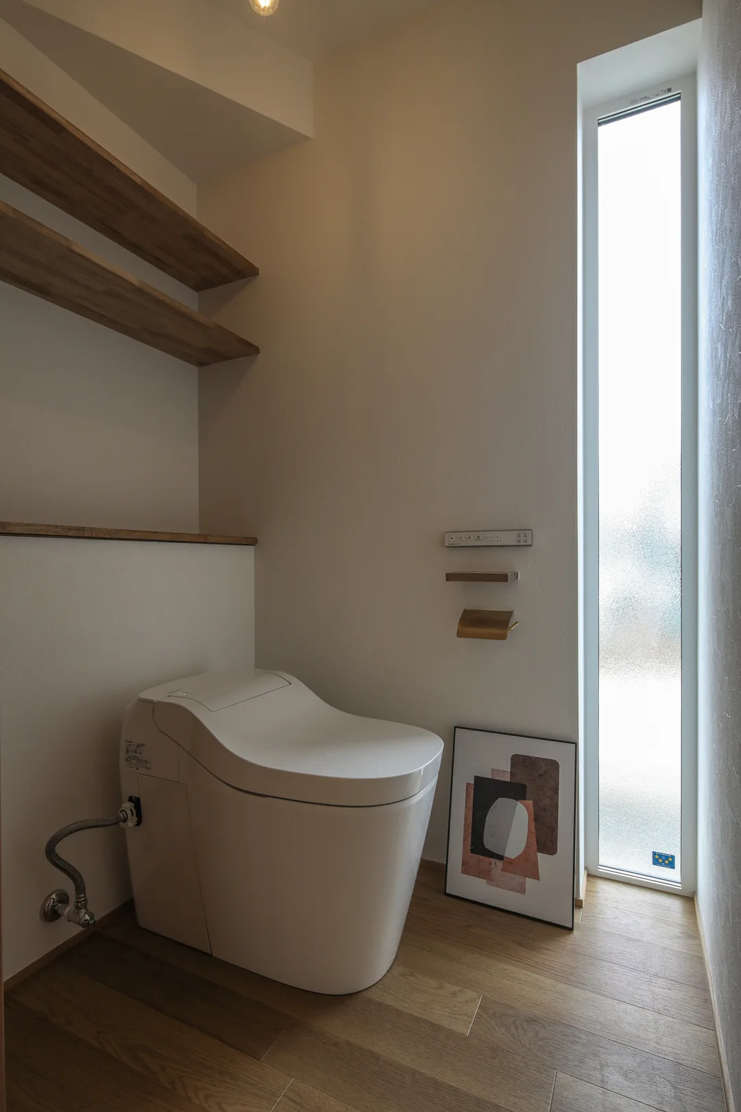 トイレ。右手奥には縦長窓。床は木目調の硬質塩ビタイル。トイレの背面上部に2枚の棚板