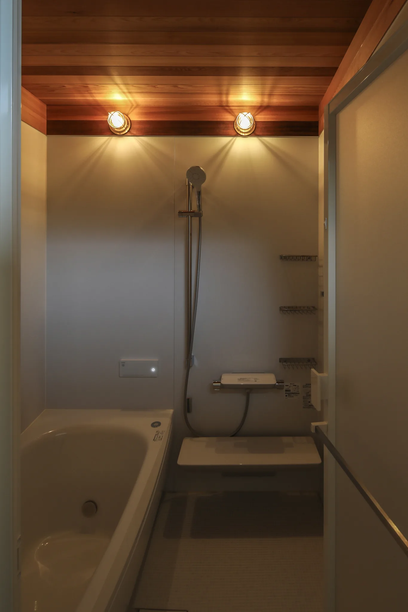 風呂の洗い場と浴槽。ユニットバスだが天井部分が造作でレッドシダーが貼られている。照明はマリンライトが2つ横に並んでついている。
