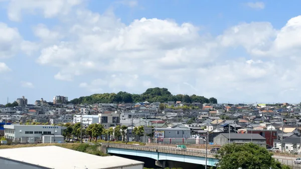 雲が浮かぶ青空の下に街並みが見える。手前には車が通る橋がある