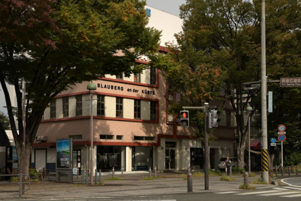 街の風景。正面に3階建ての建物があり、左右には建物より大きな樹が植わっている